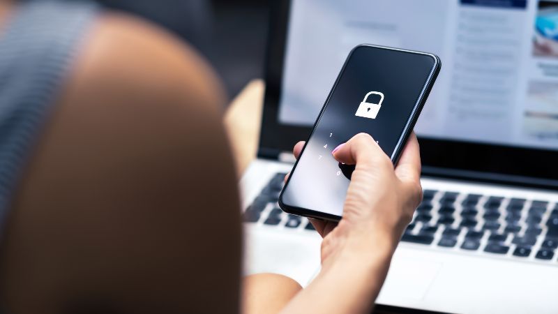 Frau mit Smartphone in der Hand vor einem Laptop.