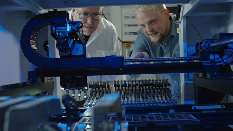 Preußner und Fastenrath sprechen vor einer Maschine mit Greifarm