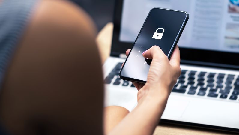 Nahaufnahme einer Frau von hinten, in der Hand hält sie ein Smartphone mit Schloss-Symbol auf dem Display